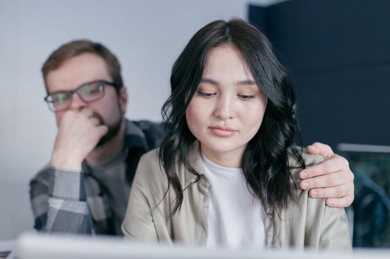 Man placing his hand on a woman’s shoulder as she works.