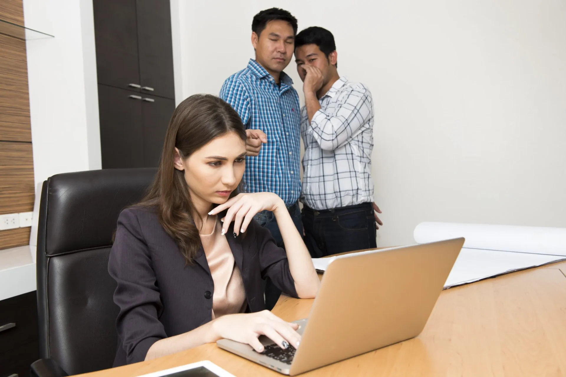 Two male employees watching over a female’s shoulder as she searches for a sexual harassment lawyer near me in Marin County, CA