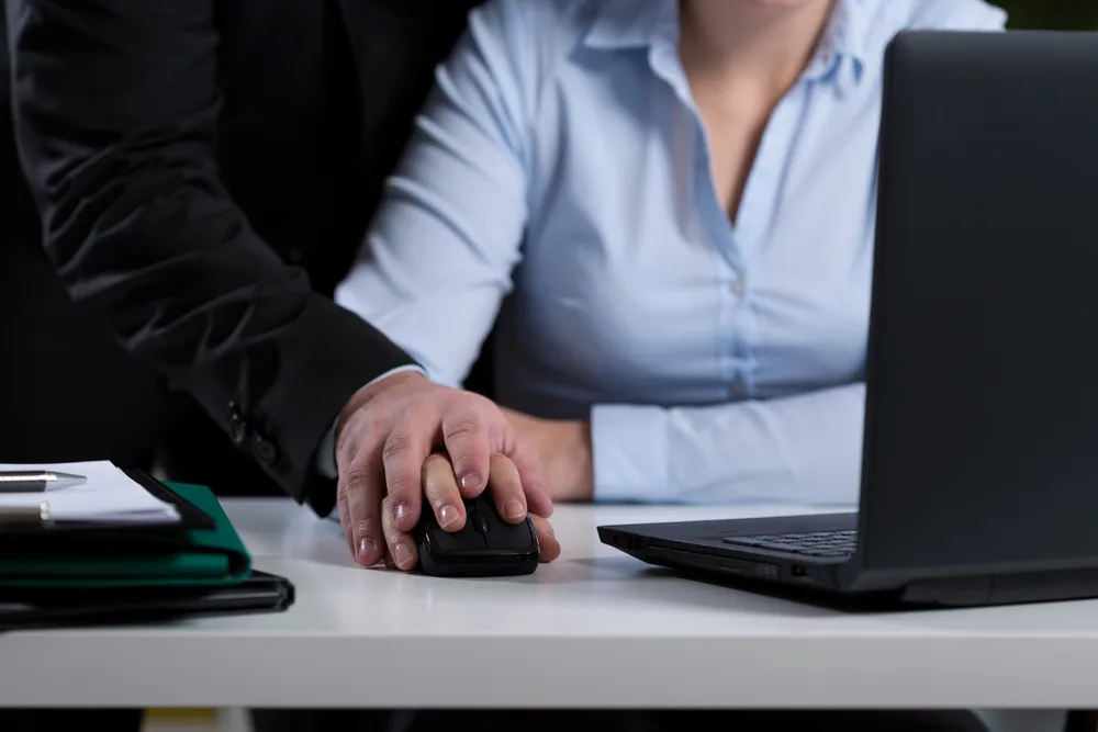 A woman preparing to contact an Oakland, CA, sexual harassment lawyer as another person puts his hand over hers