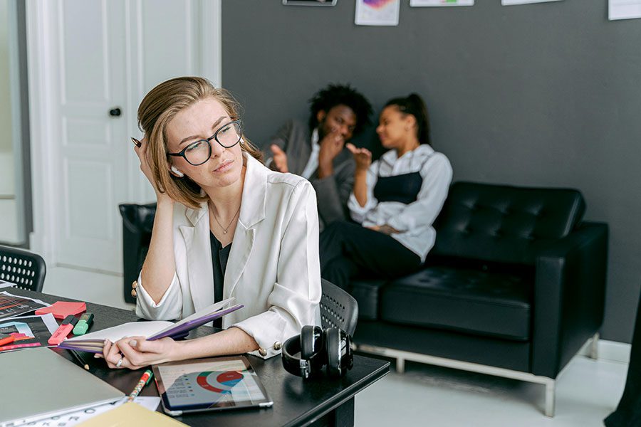 An employee sitting at her desk while her co-workers have a conversation