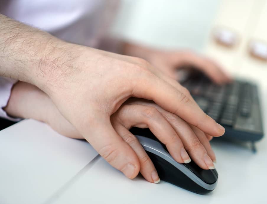 Hand of male sexually harassing a female coworker by placing his hand over her mouse hand in a San Francisco workplace.