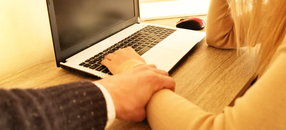 A harasser trying to stop a worker from searching for sexual harassment lawyers near me in Fresno, CA, on her laptop.